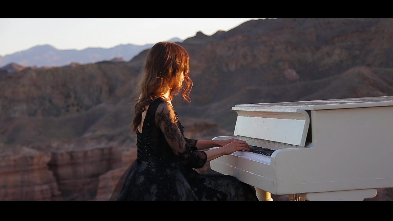 A pianist at a white grand piano against a canyon landscape
